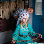 Alexander Polibza prepares Veronika to photograph her in a traditional wedding costume, in Kubey village, Ukraine, on October 26, 2023. Alexander is an enthusiastic ethnographer who collects old costumes and items and records songs and tales from all over Bessarabia. © Mihaela Aroyo / VII Mentor Program.