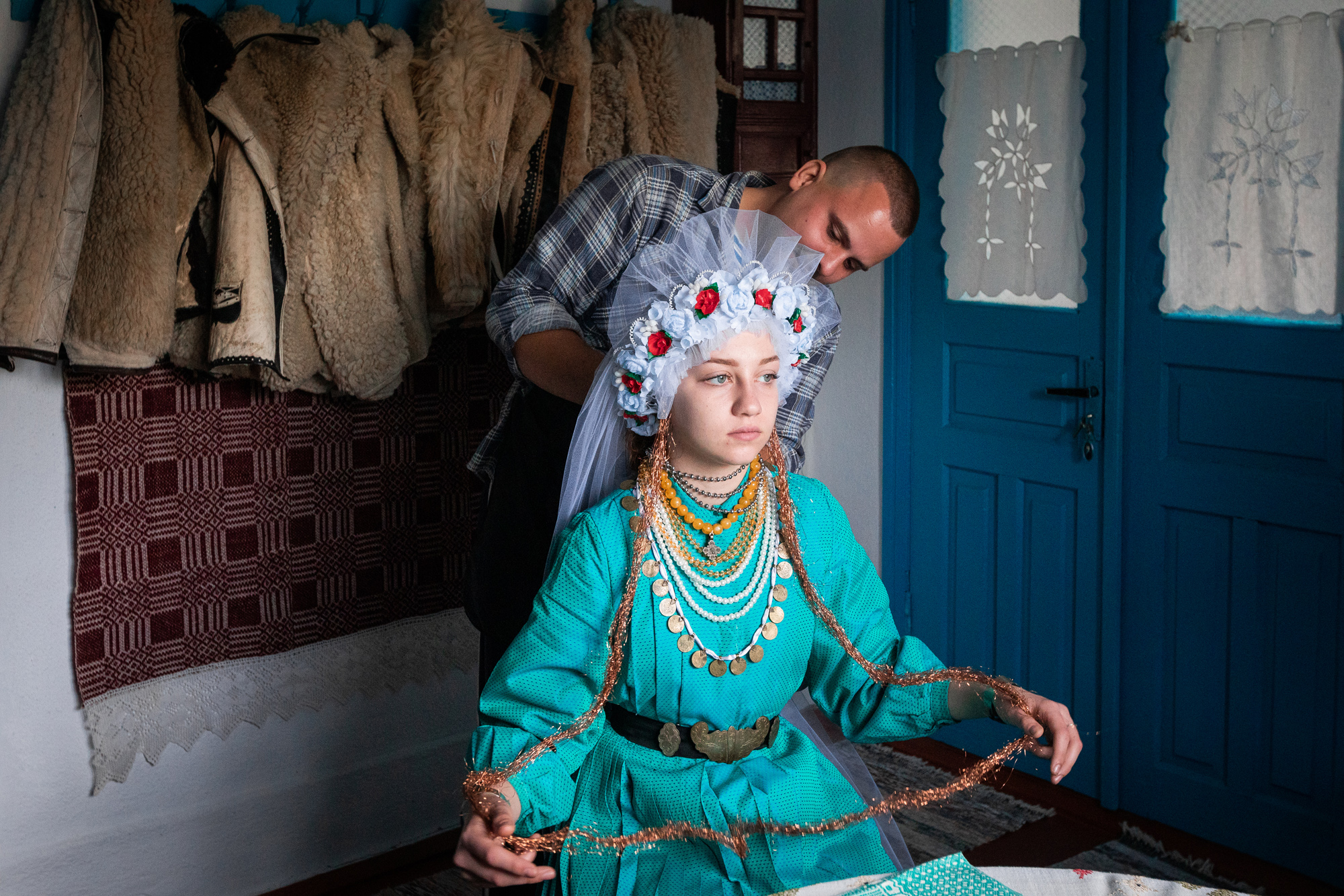 Alexander Polibza prepares Veronika to photograph her in a traditional wedding costume, in Kubey village, Ukraine, on October 26, 2023. Alexander is an enthusiastic ethnographer who collects old costumes and items and records songs and tales from all over Bessarabia. © Mihaela Aroyo / VII Mentor Program.