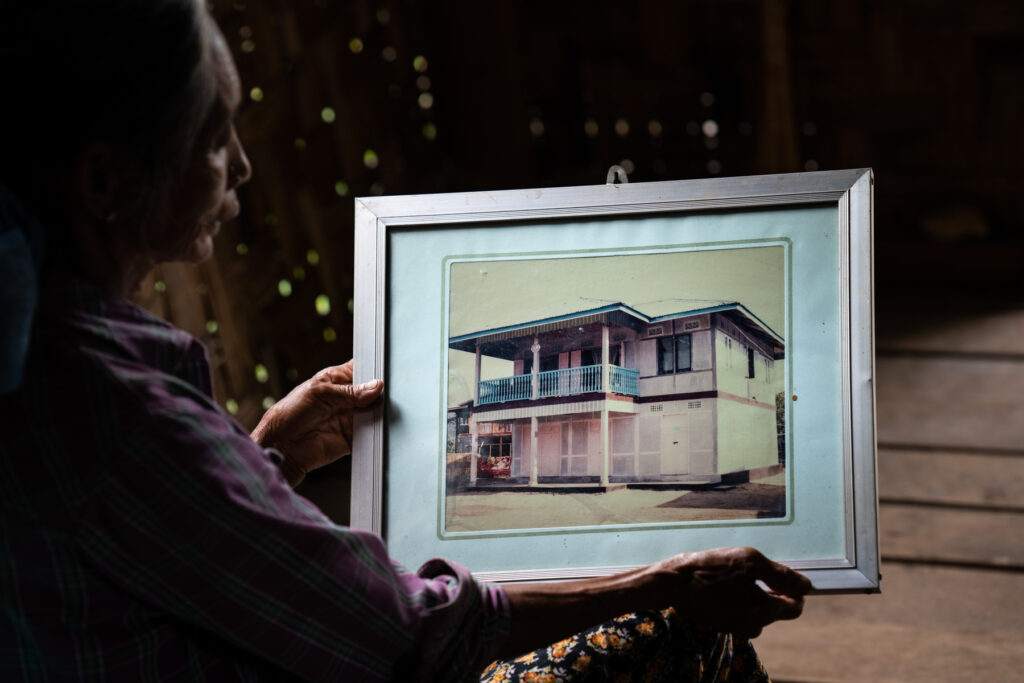 A displaced elderly woman holds a photograph of her former home, which she believes was destroyed in the conflict.