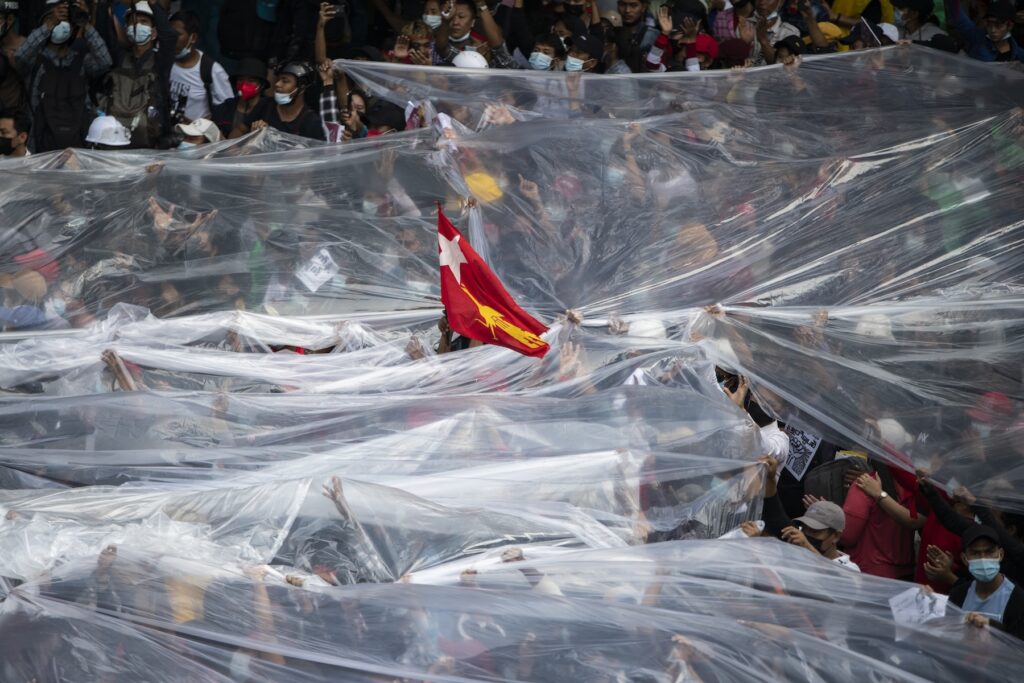 Protesters cover themselves with plastic sheets to shield themselves from tear gas during a confrontation with riot police in Yangon.